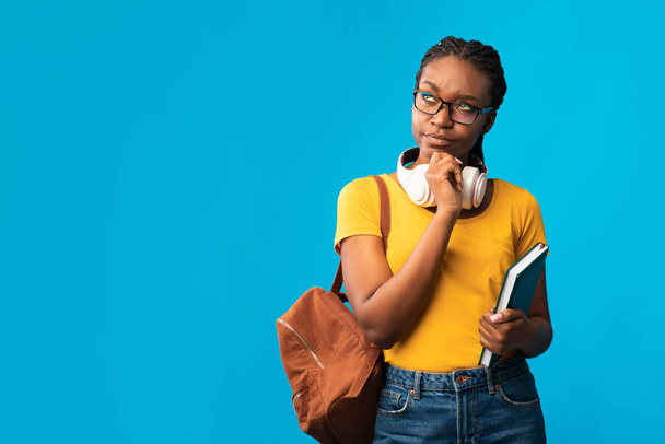 Στοχαστικό μαύρο κορίτσι φοιτητής σκέφτεται στέκεται σε μπλε φόντο στούντιο - Φωτογραφία, εικόνα