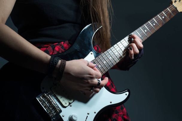 Πορτρέτο της νεαρής γυναίκας που κρατά ηλεκτρική κιθάρα σε μαύρο και άσπρο close-up γυναικεία χέρια παίζουν σκληρό ροκ εντ ρολ ρυθμική φιγούρα. Φωτογραφία στούντιο σε γκρι φόντο. Βρωμερή μουσική γκαράζ. Βαρύ στυλ punk. - Φωτογραφία, εικόνα