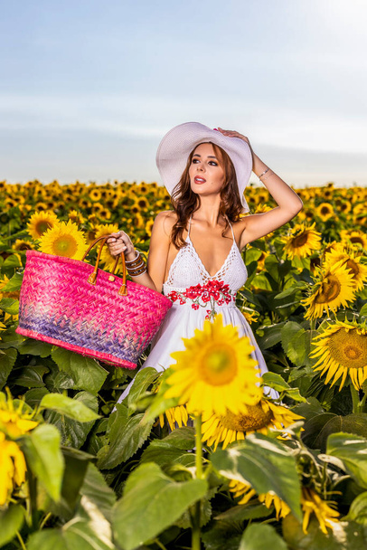 Krásná žena pózuje na zemědělském poli se slunečnicí za slunečného letního dne - Fotografie, Obrázek