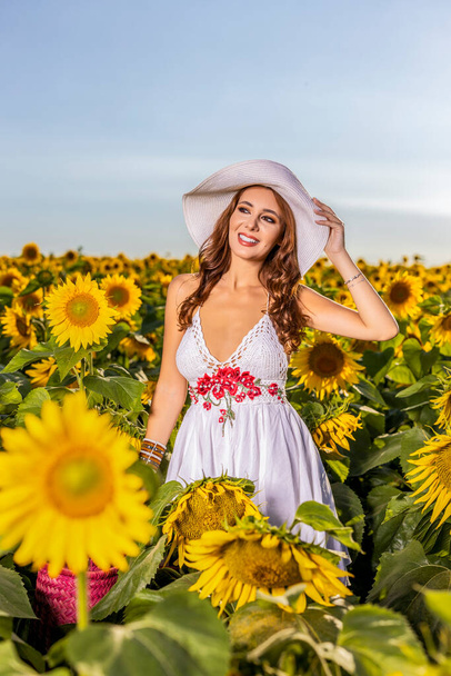 Beautiful woman poses in the agricultural field with sunflower on a sunny summer day - Zdjęcie, obraz