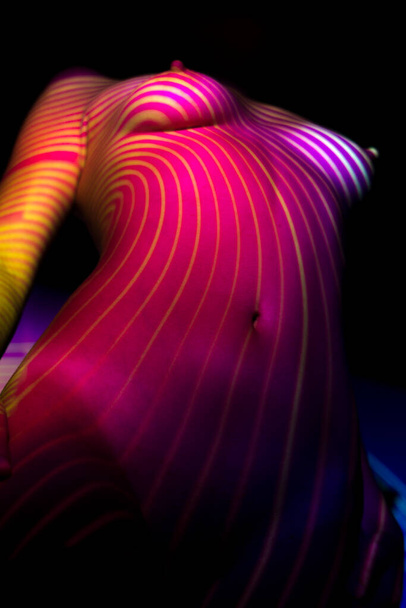 Bust of a slender white woman. Topless girl under abstract light. Bright light illuminates the naked female body. Female body bottom view. Elongated perspective. Protruding nipples. dark nipples - Photo, image