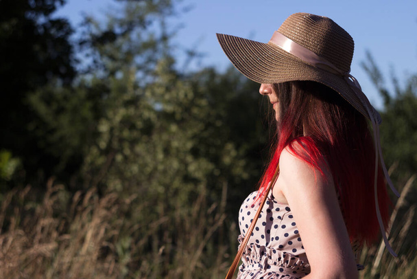 Uma jovem mulher bonita com cabelo vermelho vestido com um vestido bege em bolinhas pretas está entre o campo. Verão, fundo
 - Foto, Imagem
