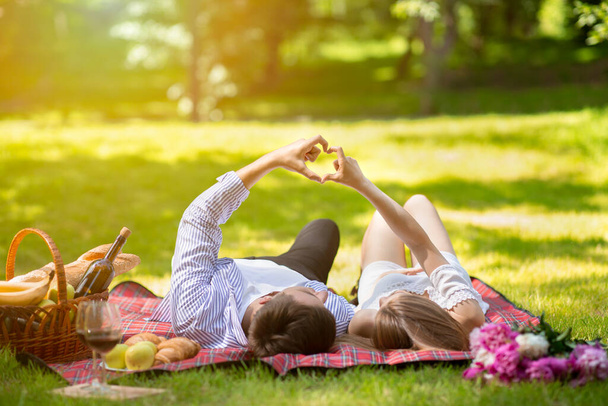 Yaz aylarında parkta piknik yaparken sevgi dolu bir çift elleriyle kalp yapıyor. - Fotoğraf, Görsel