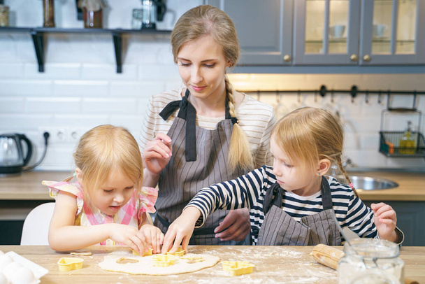 Happy family mom and two cute daughters preparing homemade cookies in the kitchen. - Fotografie, Obrázek