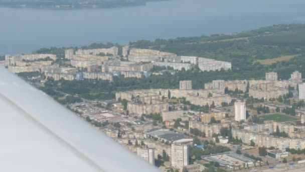 Matkustajatason valkoinen siipi suuren asuinrakennuksen taustaa vasten, monikerroksiset rakennukset lentokoneen ikkunan ylhäältä - Materiaali, video