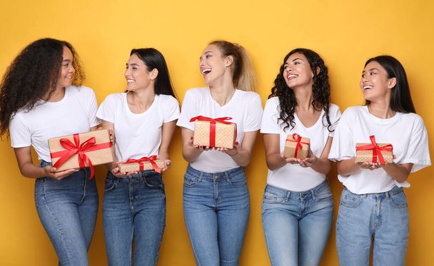 Fröhliche Freundinnen halten verpackte Geschenkboxen über gelbem Hintergrund - Foto, Bild
