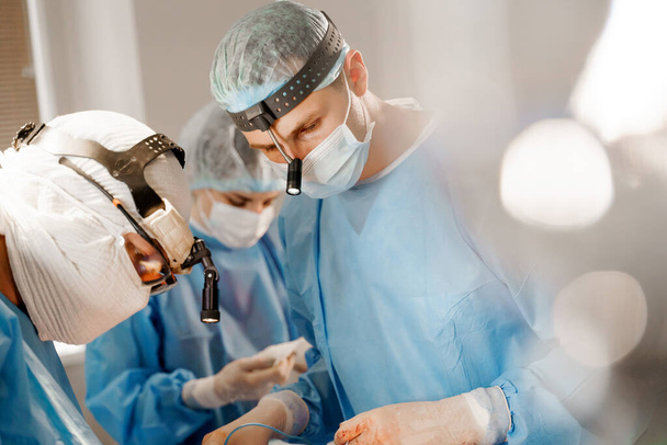Хірург вставляє силіконові імплантати в груди жінки. Цицьки доповнення пластику операція і корекція в медичній клініці. Група професійних медиків в медичних масках і рукавичках роблять пластичну хірургію
. - Фото, зображення