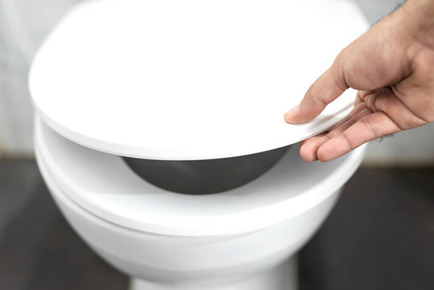 Мужчина открывает сиденье унитаза рукой в ванной комнате
 - Фото, изображение