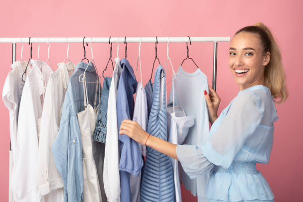 Portrait of cheerful girl choosing clothes standing near rack - Φωτογραφία, εικόνα
