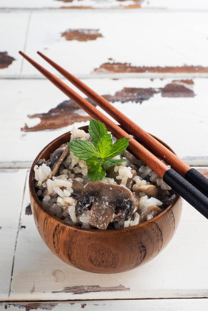 Risotto with mushrooms on a wooden plate and chopsticks. Boiled white rice with champignons in cream sauce. Light wooden background. Copy space - Foto, imagen