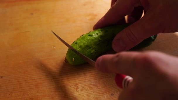 Mens hands slice fresh cucumber on a wooden board - Metraje, vídeo