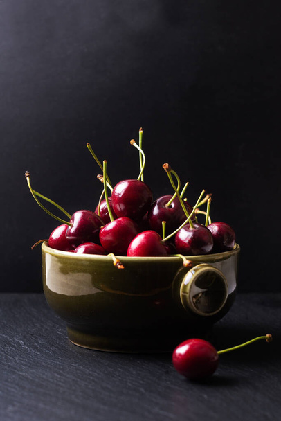 Summer food concept organic fresh cherry fruits in green cup on black slate board background with copy space - Photo, Image