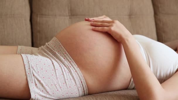 Een zorgzame moeder streelt een naakte zwangere buik met twee handen, op lichte kamer. Een zwangere vrouw streelt een grote buik in de zonnige zomerdag. - Video