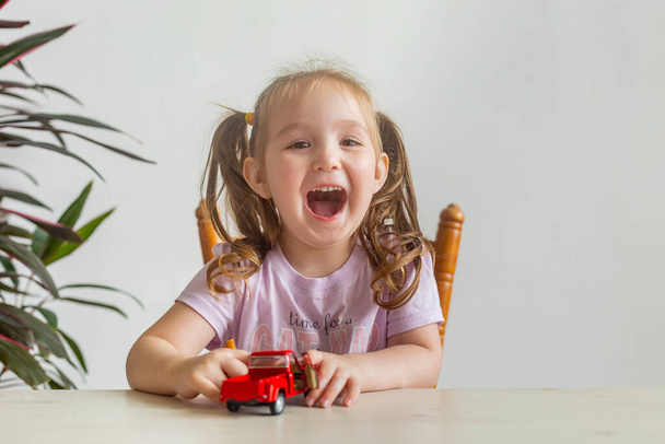 Little cute girl playing with a small red toy car.  Healthy happy toddler with colorful red car indoors. Little girl laughs - Фото, зображення