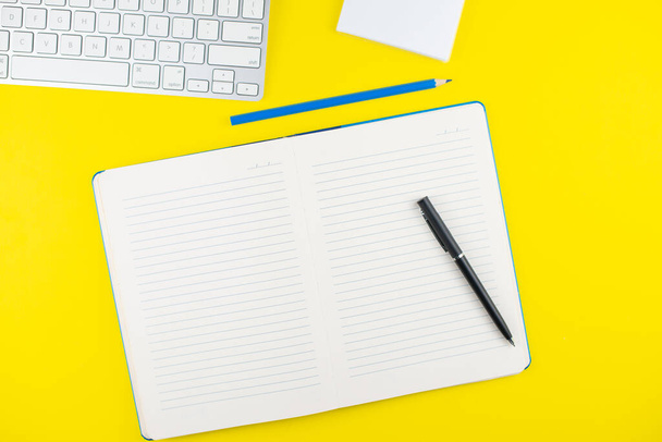 Black pen, notepad planner, pencil and keyboard on yellow background. Flat lay. Copy space. Workplace in the office.  - Photo, image
