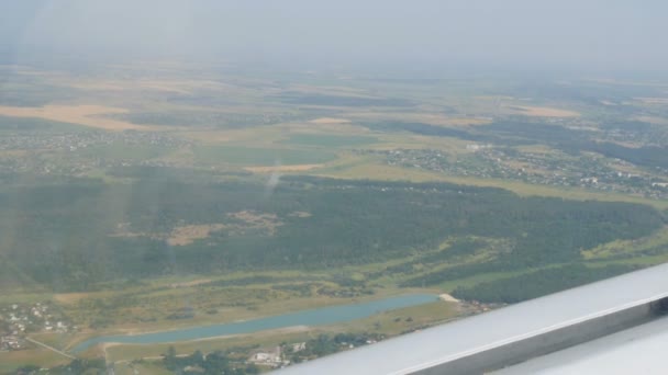 Біле крило пасажирського літака на тлі красивого блакитного озера, летить над ставком, зеленими лісами і маленькими будинками і містечками. Концепція подорожей
 - Кадри, відео