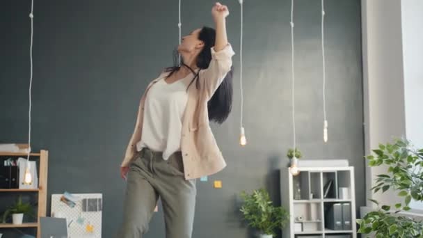 Slow motion of cheerful business lady dancing on table in modern office enjoying music - Video