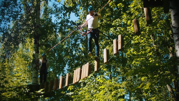 Homem cruzando uma construção da corda e tocos - uma atração de entretenimento na floresta verde
 - Foto, Imagem