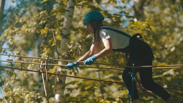 Una mujer con casco cruzando el puente de cuerda - una atracción de entretenimiento en el bosque
 - Foto, Imagen