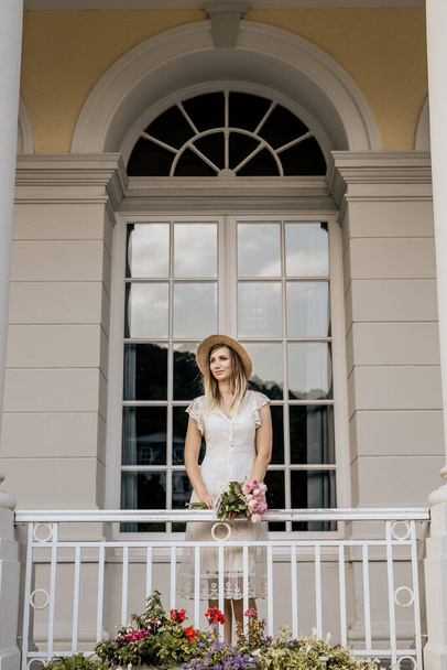 Portrait of blond woman in white dress. Beautiful girl stay on balcony at home - Foto, imagen