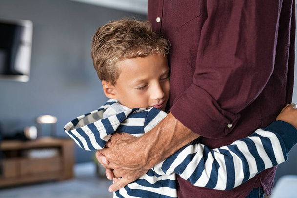 Grandchild giving a warm hug to grandfather at home. Attached cute little boy embracing senior man at home with copy space. Young grandson with closed eyes feeling relieved on hugging old granddad.  - Fotoğraf, Görsel