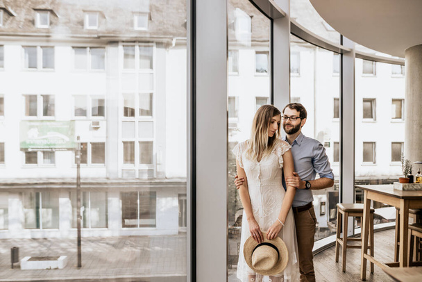 Романтическая пара возле панорамных окон в ресторане. Счастливая семья в объятиях
 - Фото, изображение