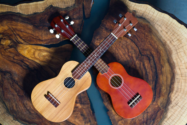 Dwa ukulele w różnych kolorach - jasny i ciemny brąz na pięknym drewnianym stole. - Zdjęcie, obraz