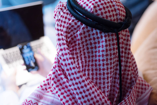 中東のビジネスマンは電話で話し、彼のオフィスの窓の外を見ています。通信に接続するために携帯電話を使用してビジネスマンアラビア語. - 写真・画像