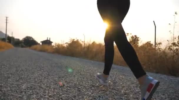 Stopy zdrowej dziewczyny biegającej po wiejskiej drodze ze wschodem słońca w tle. Kobiece nogi biegające na zewnątrz. Nierozpoznana sportowa kobieta ćwicząca wczesnym rankiem. Koncepcja aktywnego stylu życia. Zwolniony ruch - Materiał filmowy, wideo