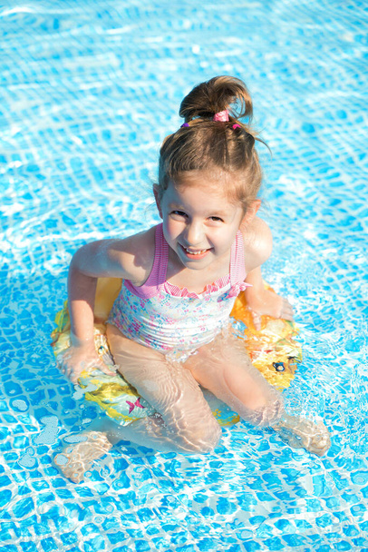 Funny little girl swims in the pool in a yellow lifebuoy - Photo, Image