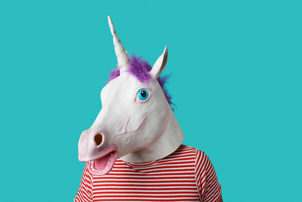 man wearing a unicorn mask and a red and white striped t-shirt on a blue background with some blank space around him - Foto, afbeelding