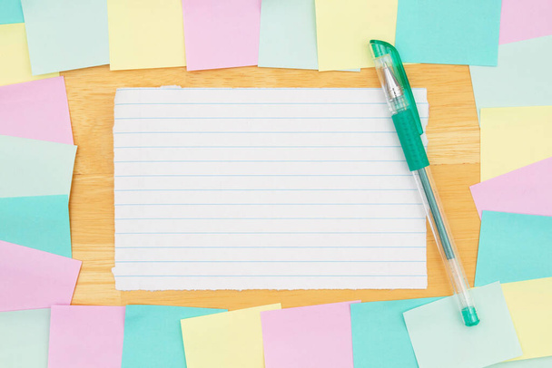 Klebriger Notizhintergrund mit mehrfarbigen Notizen und einem Stift auf einem Holz-Schreibtisch mit Kopierraum für Ihr Büro oder Ihre Erinnerungsnachricht - Foto, Bild