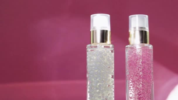 Πολυτελή προϊόντα περιποίησης του δέρματος και λαμπερές φωτεινές φωτοβολίδες σε ροζ φόντο, βάση μακιγιάζ και τζελ ορού ως ρουτίνα φροντίδας του δέρματος για καλλυντικά προσώπου και μάρκα ομορφιάς - Πλάνα, βίντεο