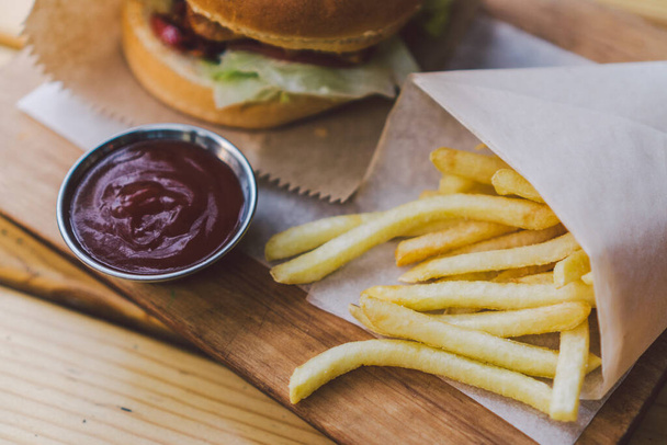 Fresh tasty burger and french fries on wooden table. french fries and bbq sauce on wood plate. street food burger and fried potatoes. Unhealthy food. fast food and unhealthy eating concept. - Photo, Image
