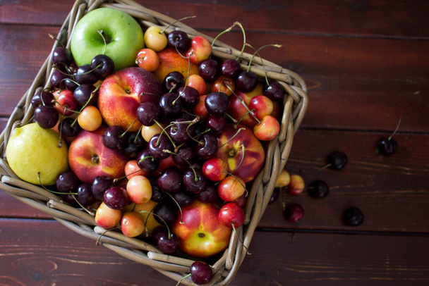 Kesähedelmät korissa puupöydällä. Vilkas värit kauniita kirsikoita, omenoita ja nektariineja. Terveellistä syömistä. Tuoreet hedelmät lähikuva kuva.  - Valokuva, kuva