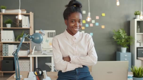 Portrait of Afro-American girl office worker smiling with arms crossed in workplace - Séquence, vidéo