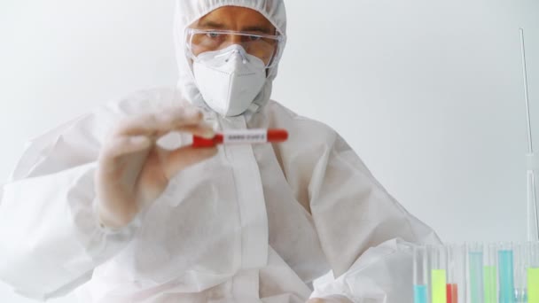 Arzt im Schutzanzug zeigt infiziertes Sars-CoV-2-Reagenzglas - Filmmaterial, Video
