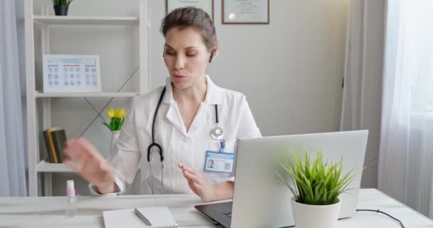 Doctor shows how to use hand sanitizer, using computer. Female medical Therapist wears medical gown, headset video calling distant patient on laptop. Telemedicine remote healthcare services concept - Filmmaterial, Video