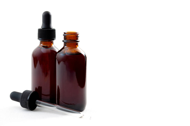 Homeopathische remedie en vloeibare tinctuur medicijnen concept met close-up op twee bruine geneeskunde glazen flessen, een open en een gesloten met druppelaar geïsoleerd op witte achtergrond met kopieerruimte - Foto, afbeelding