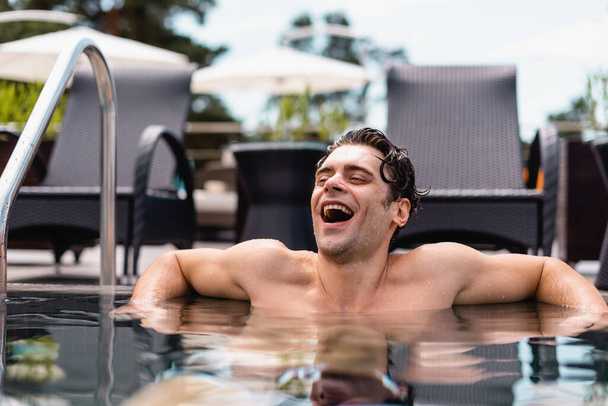 selective focus of excited and wet man laughing in swimming pool  - Foto, imagen