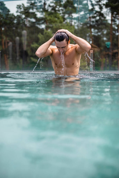 selektivní zaměření mokrého a svalnatého muže dotýkajícího se vlasů v bazénu - Fotografie, Obrázek