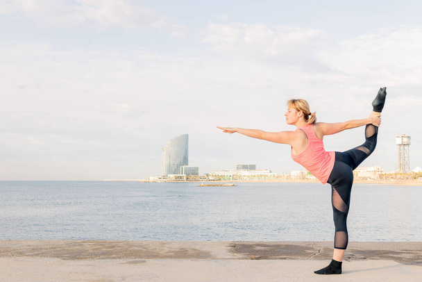 mooie sportvrouw beoefenen van evenwicht en yoga strekt zich bij dageraad in de voorkant van de zee, concept van geestelijke gezondheid en ontspanning, kopieer ruimte voor tekst - Foto, afbeelding