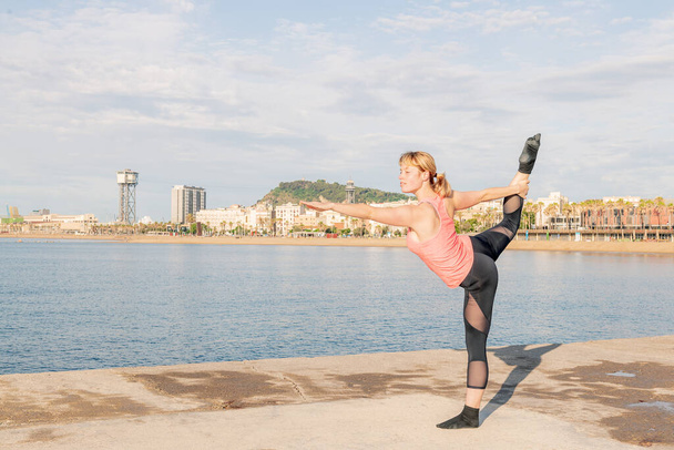 blonde sportswoman practicing balance and yoga stretches in front of the sea, concept of mental health and relaxation, copy space for text - Foto, immagini
