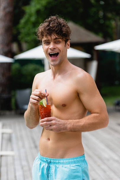 excited and shirtless man holding glass with cocktail  - 写真・画像