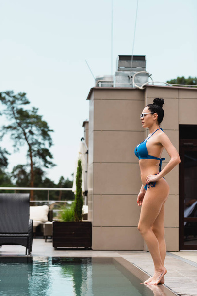 barefoot woman in sunglasses standing near swimming pool  - Valokuva, kuva