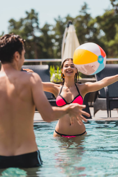 messa a fuoco selettiva di ragazza e uomo a torso nudo giocare a pallavolo con pallone da spiaggia in piscina  - Foto, immagini