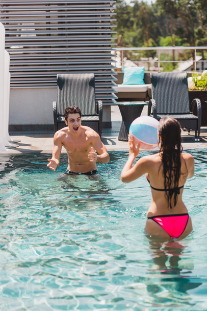 back view of woman and shirtless man playing volleyball with beach ball in swimming pool  - Foto, Imagem
