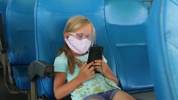 Девочка в защитной маске использует смартфон - Кадры, видео