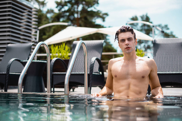 επιλεκτική εστίαση του υγρού και μυϊκού άνδρα κοιτάζοντας κάμερα στην πισίνα - Φωτογραφία, εικόνα