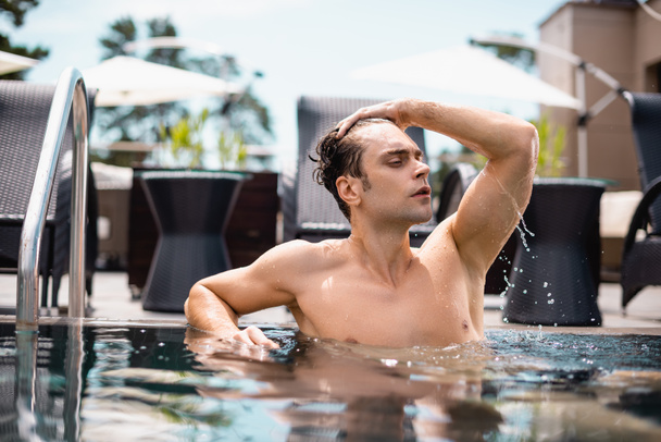 shirtless man looking away and touching wet hair in swimming pool  - Photo, Image